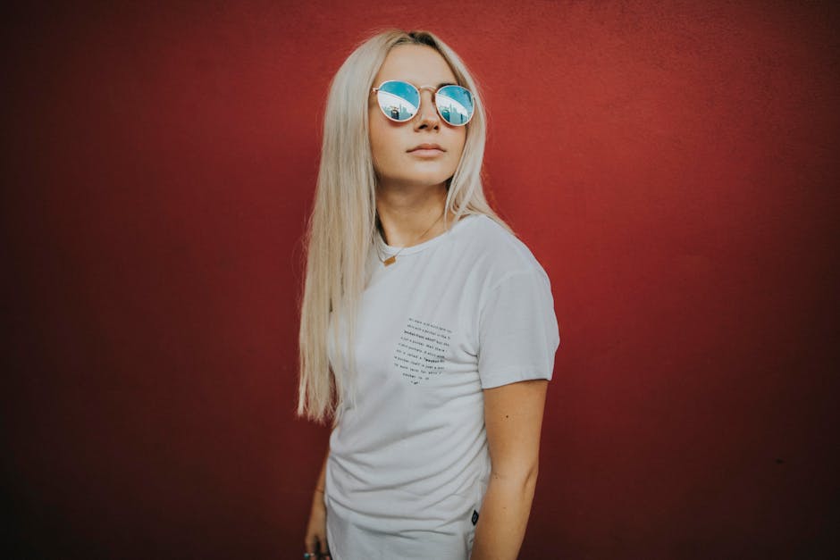 Stylish woman with blonde hair and sunglasses posing against a red background.