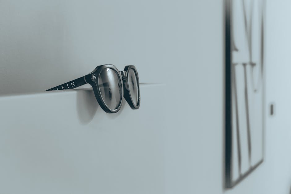 Close-up of black sunglasses resting on a minimalist white wall, fashion-focused decor.