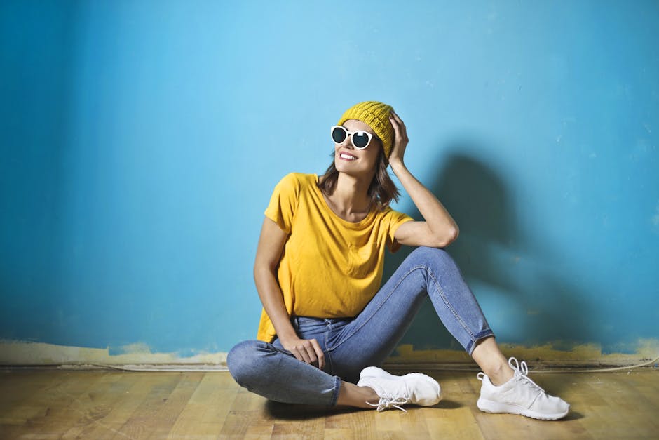 Casual woman in yellow posing against a blue wall with a joyful expression.