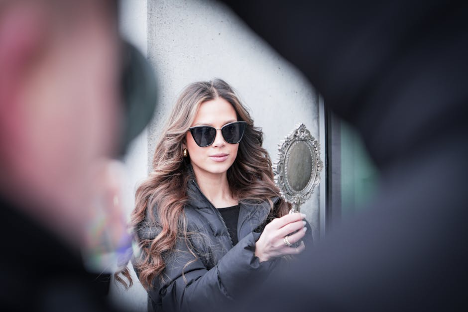 Fashionable woman with sunglasses uses handheld mirror on a Berlin street.
