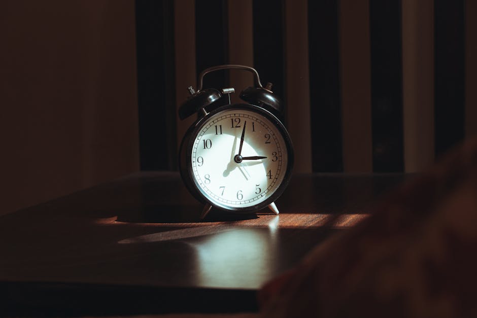 An antique black analog alarm clock casting shadows on a wooden table, exuding a nostalgic, moody ambiance.