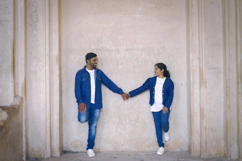 A happy couple in matching blue denim standing and holding hands against a textured wall.